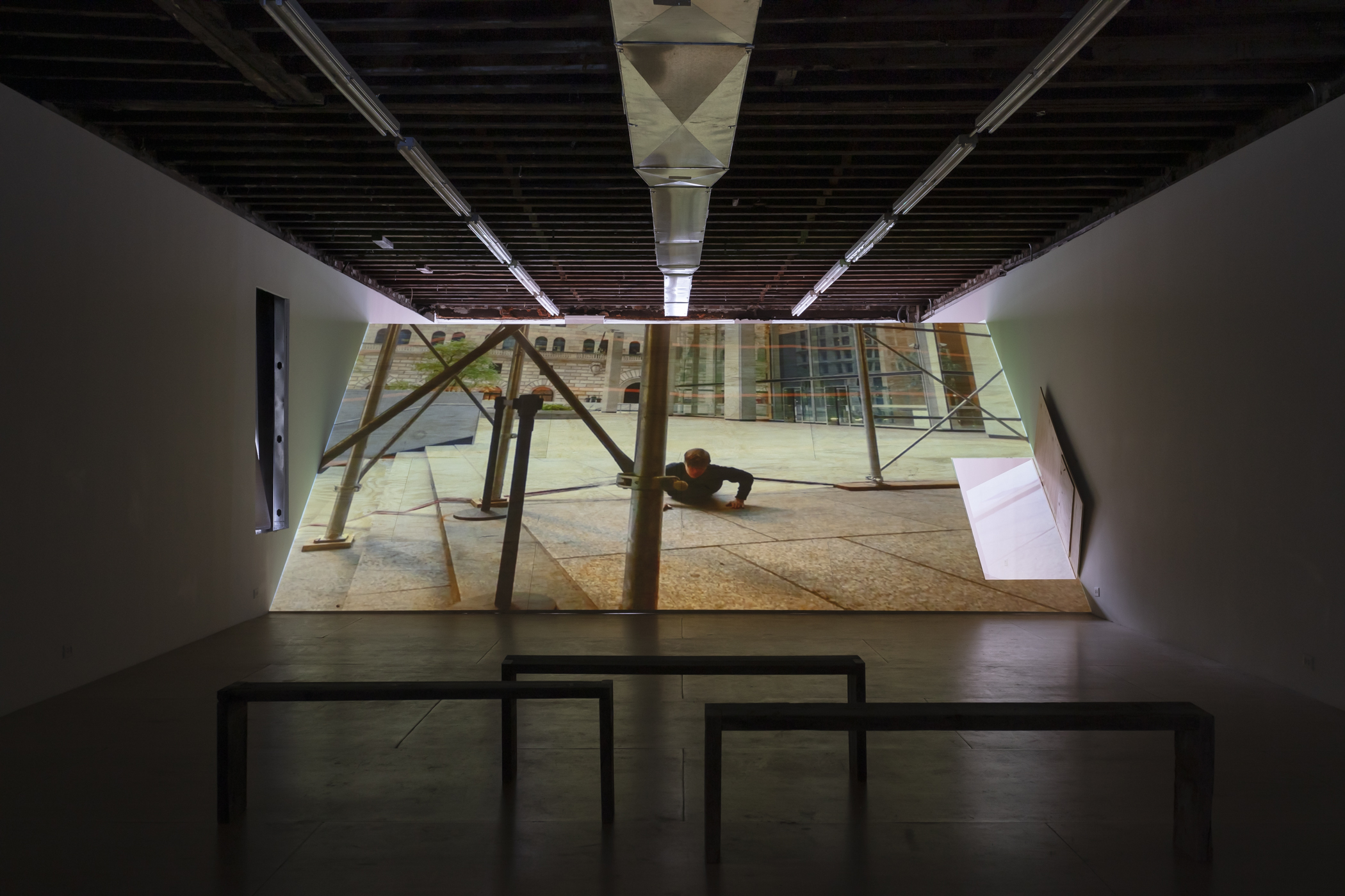 video still of artist falling on pavement projected onto wooden ramp