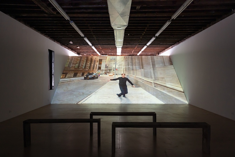 video still of artist falling on pavement projected onto wooden ramp